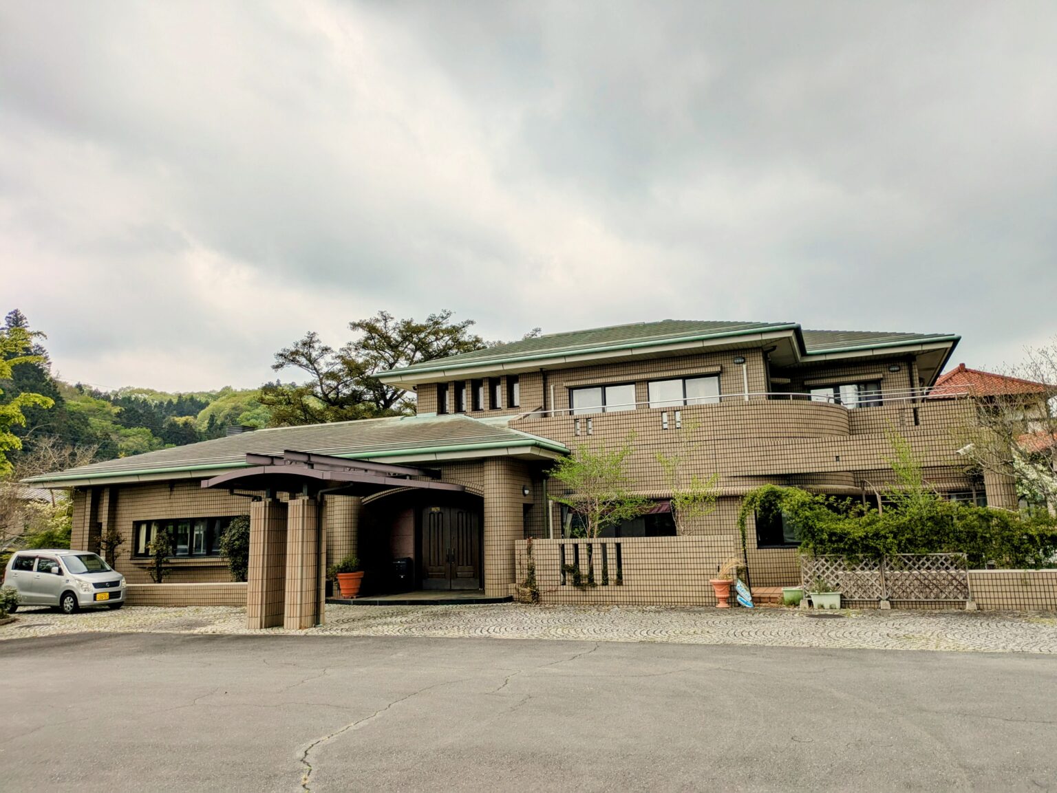 緑色の屋根を持つ大型介護施設の建物外観。駐車場と玄関ポーチが見える。